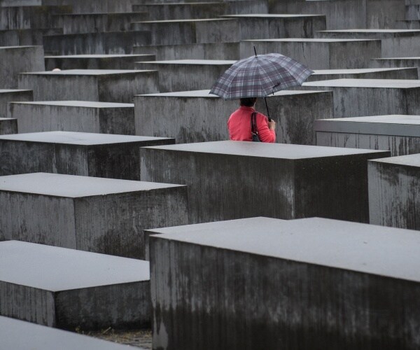 woman in pink with gray umbrella walks in holocaust memorial