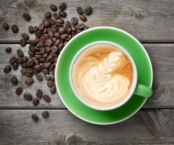 green coffee cup of cappuccino with coffee beans on table