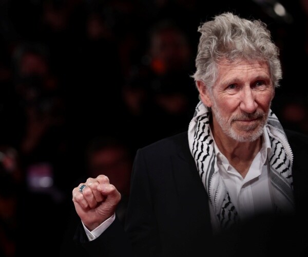 waters in a black suit and black and white scarf with a white shirt