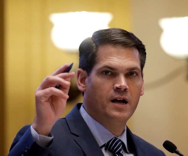 duncan in a suit and light blue shirt speaking while holding a pen