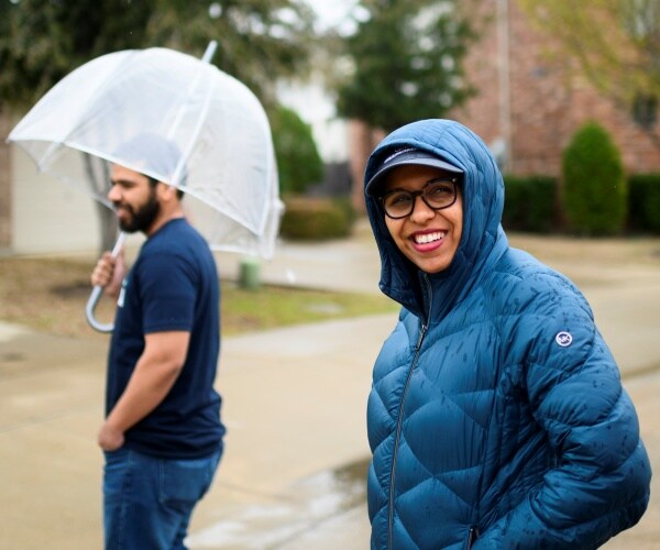 candace valenzuela in a blue waterproof jacket walking in a neighborhood with her husband under an umbrella