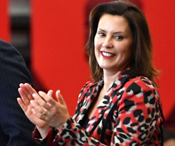 Gretchen Whitmer looks to her left toward the camera and claps and smiles