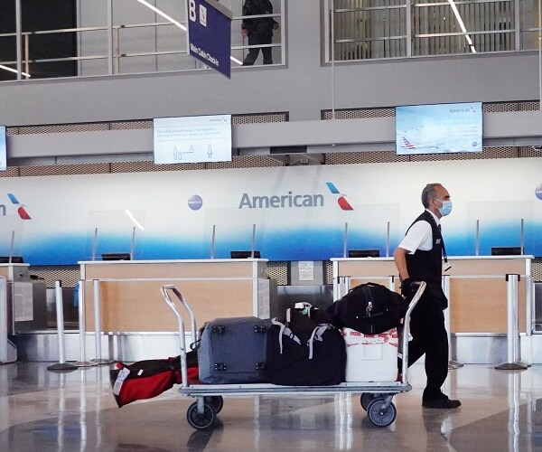 worker wheels luggage cart across airport