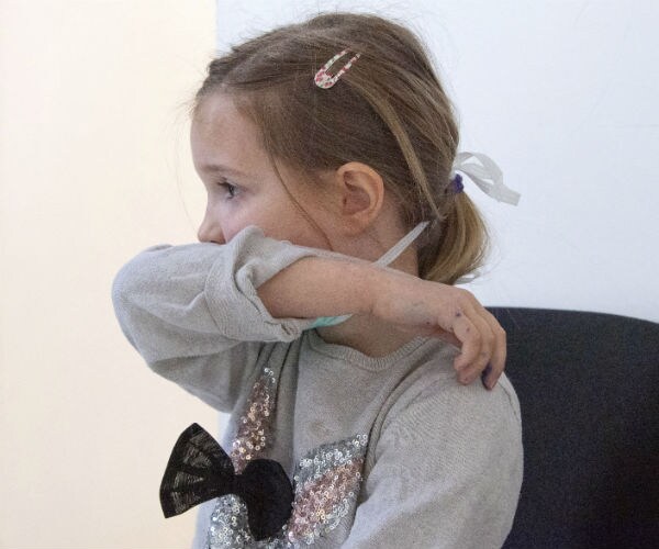 a child is shown coughing into her sleeve