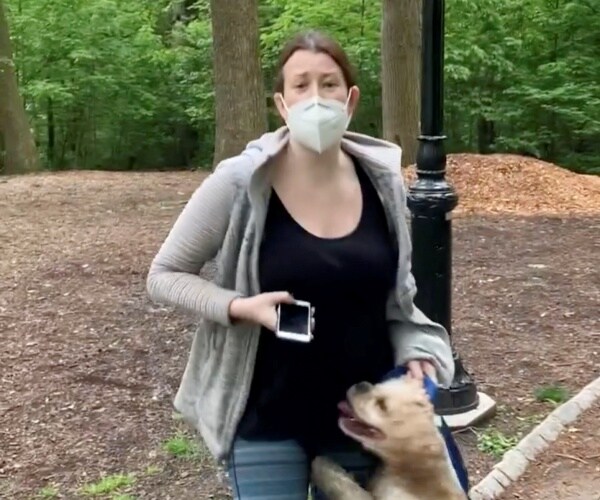 cooper in a black tank top and face mask holds her phone and stands with her dog