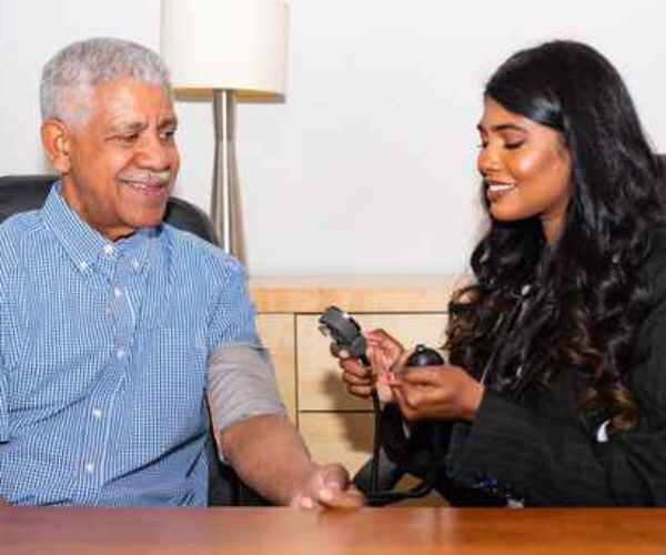 an older black male, sitting in a chair, is examined by a doctor