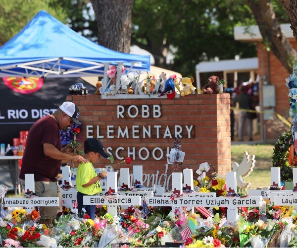 a man and child in front of the sign  for robb elementary school covered in flowers