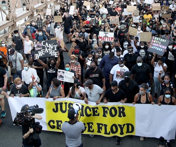 black americans protest and hold up signs with a large justice for floyd banner held up in the front