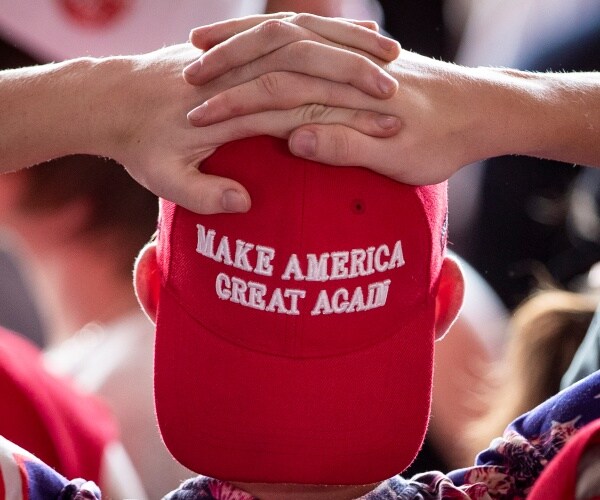 man wears a maga hat and clasps his hands on his head