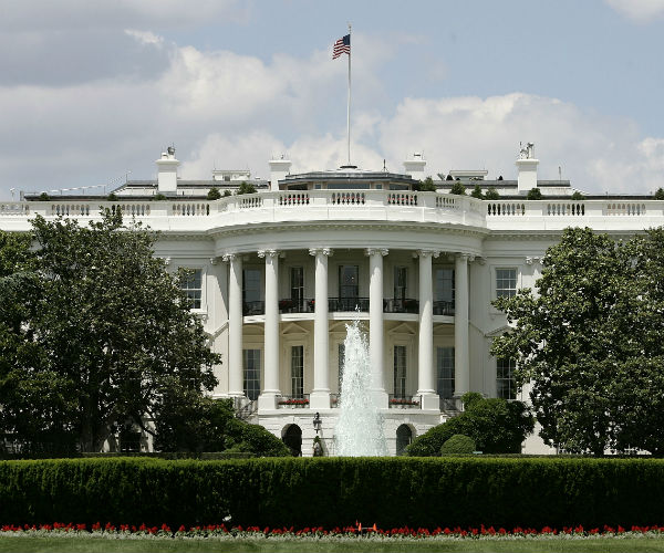 an american flag sits atop the white house in front of a cloud-peppered blue sky