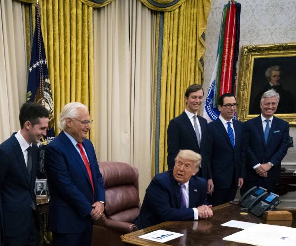 trump seated at desk with others standing on either side of him