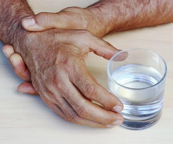 man holding hand to stop from shaking while picking up glass of water