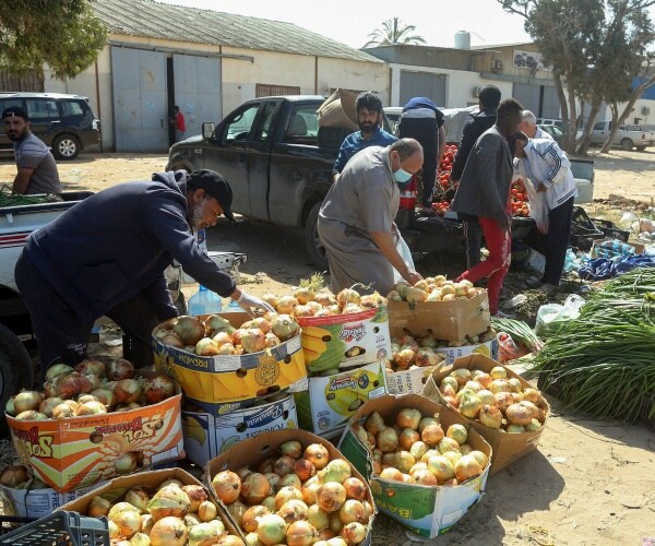 libyans buying vegetables, mostly onions, in a small market with one man wearing a mask