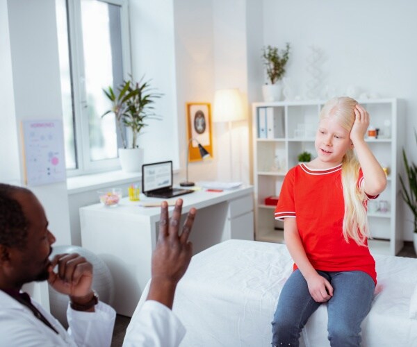 young girl on examination table looking at doctor holding up 3 fingers, testing her for concussion