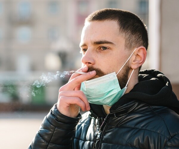 man smoking with mask pulled down onto his chin