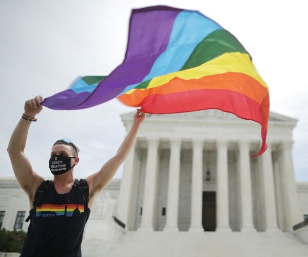 man holds a rainbow flag in front of the supreme court