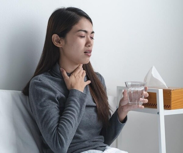 girl in bed with glass of water and holding her throat in pain