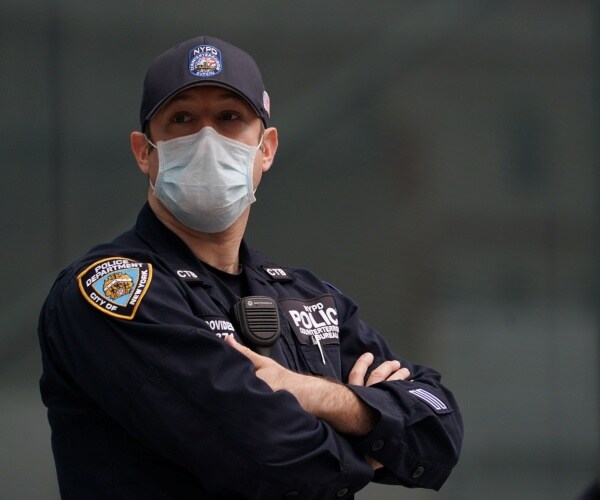 nypd officer stands wearing a black uniform, hat and face mask