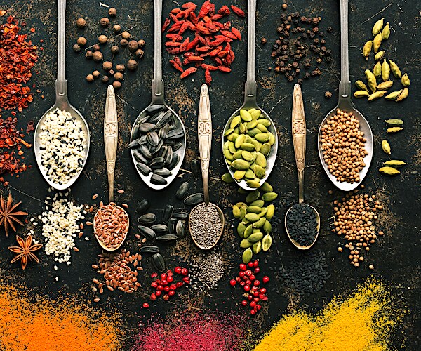 A set of varied seeds and spices in spoons on a dark background. Top view, flat lay