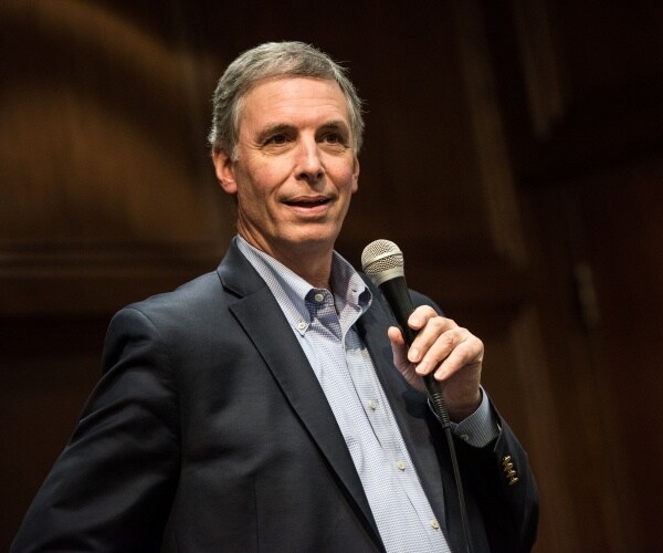 rice in a black suit and light blue shirt holding a mic