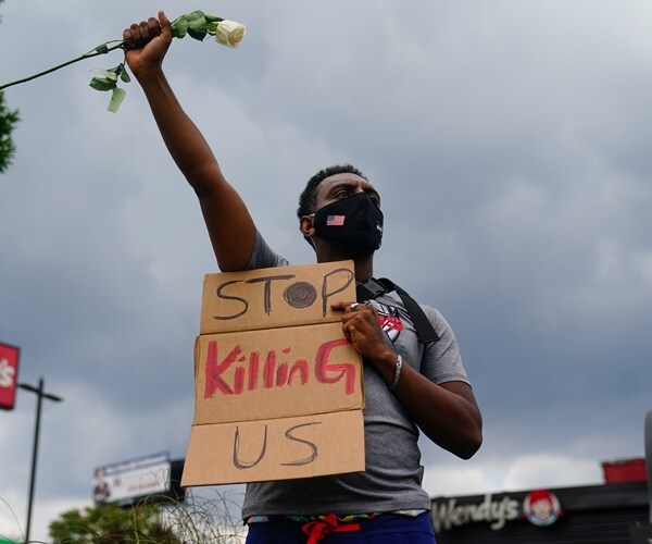 a man holds a sign and a white rose outside the wendy's where rayshard brooks was killed