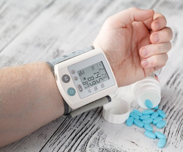 a man's arm with a monitor showing high blood pressure, and pills on the table