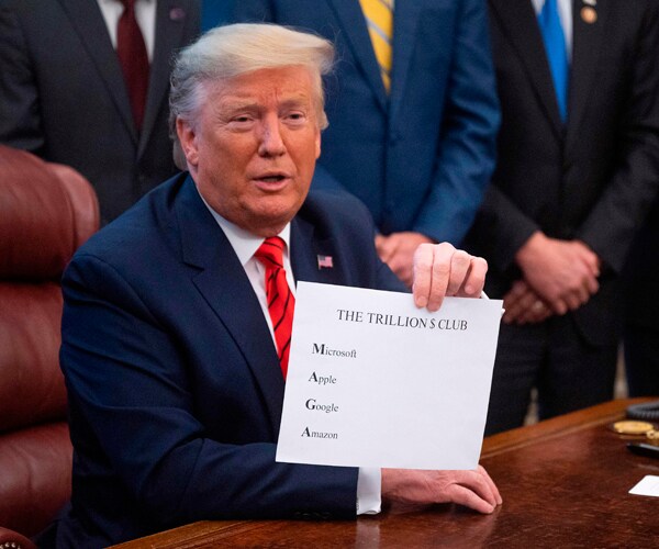 president donald trump holds up a sign that lists microsoft, apple, google, and amazon