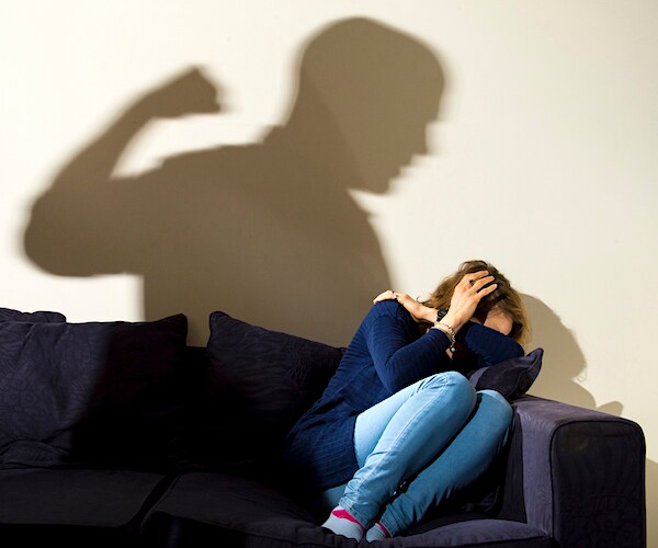 a man's shadow is cast on the wall with a woman cowering in the corner of her couch in fear
