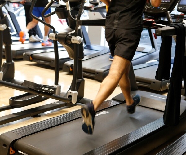 man wearing a black shirt and shorts running on a treadmill inside a gym