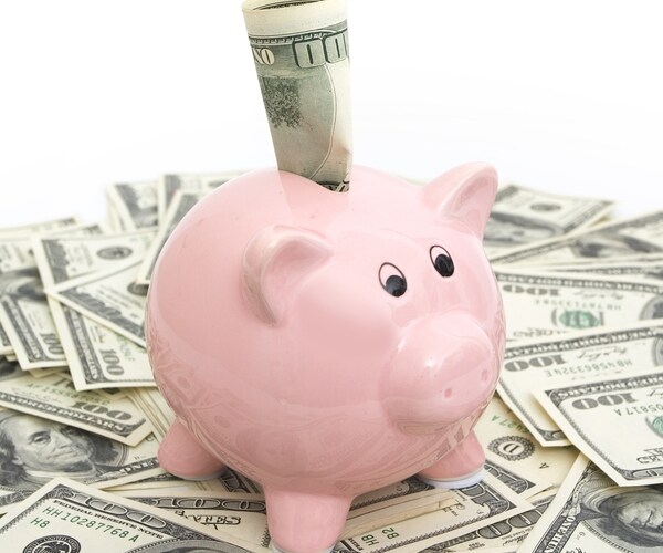 Pink piggy bank sitting on top of hundred dollar bills