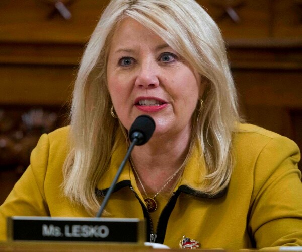 debbie lesko in a yellow/mustard dress with bright lipstick speaking into a microphone