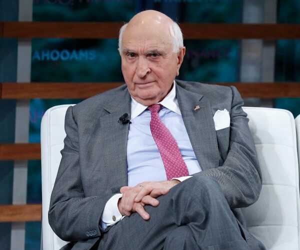 langone in a gray suit and pink polka dotted tie sitting on a white couch