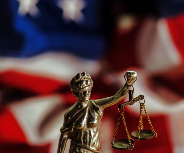 small statue of lady justice in front of an american flag