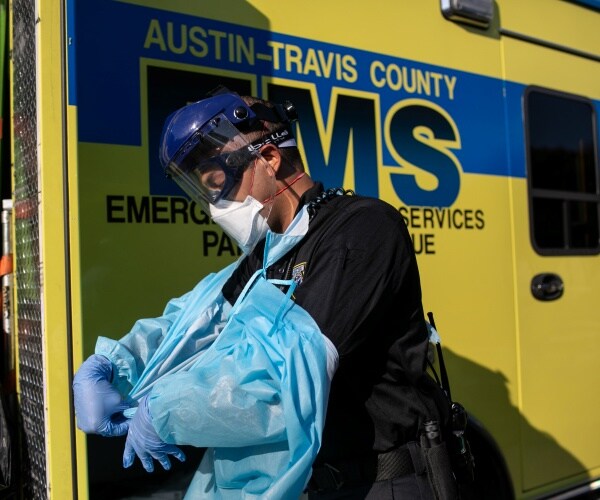 health workers in ppe roll a guerney out of an ambulance