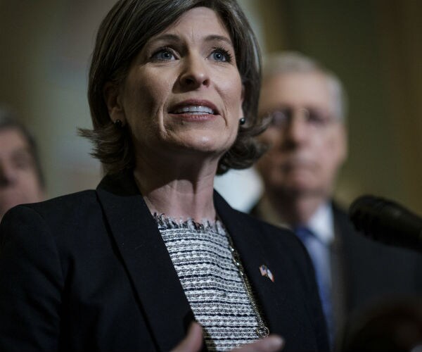joni ernst is shown black jacket and black and white blouse with a us flag pin on her lapel.