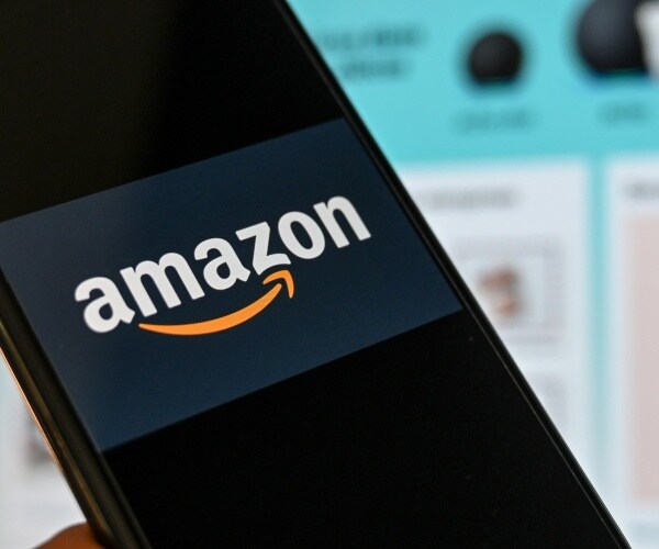 amazon logo is shown on a smartphone with site in the background