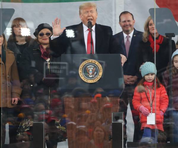 trump speaking behind a podium surrounded by other people
