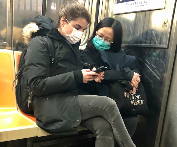 two women ride the new york city subway while wearing surgical masks