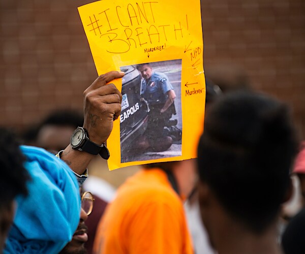a protester holds up a photo of derek chauvin holding down george floyd