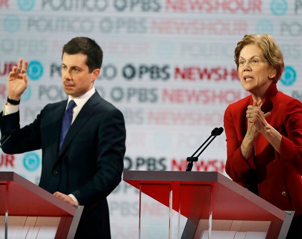 pete buttigieg raises his hand while elizabeth warren speaks during a democratic presidential primary debate