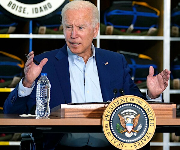 a seated joe biden grimaces as he delivers press conference remarks