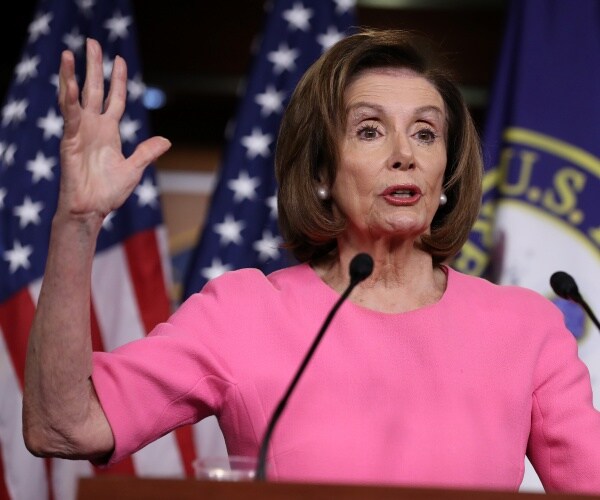 nancy pelosi wearing a pink dress raising her right hand addressing coronavirus