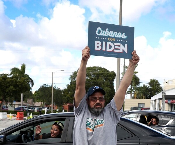 a man from the south florida latin community holds up a cubanos con biden sign.