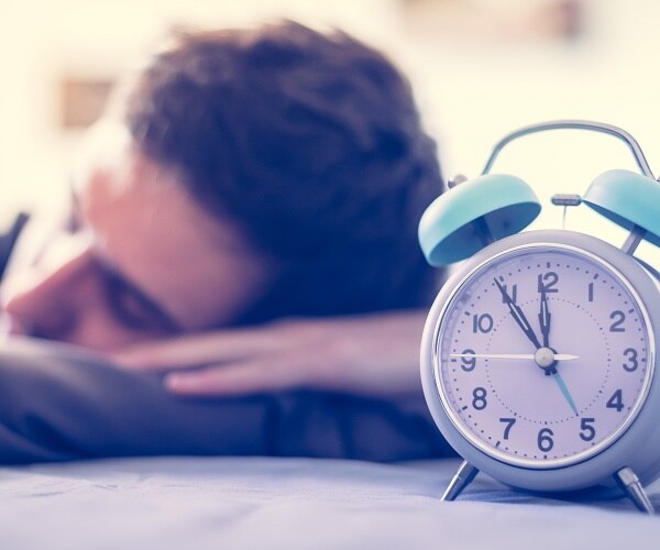 young man sleeps behind clock