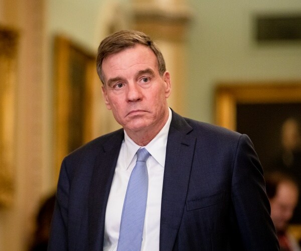 mark warner wearing a suit and light blue tie looking to the side of the camera