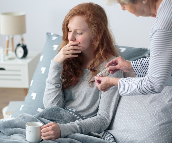 grandmother taking temperature of young girl sick with stomach bug