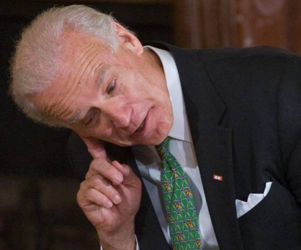 joe biden leans down with his finger to his ear