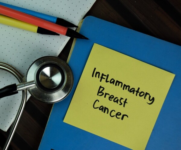 'inflammatory breast cancer' written on a yellow post-it note, on a blue folder, other folders, pens, stethoscope