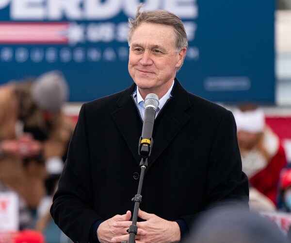david perdue smiles while standing behind mic