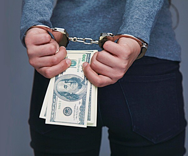 man hands in handcuffs behind back holding wad of cash